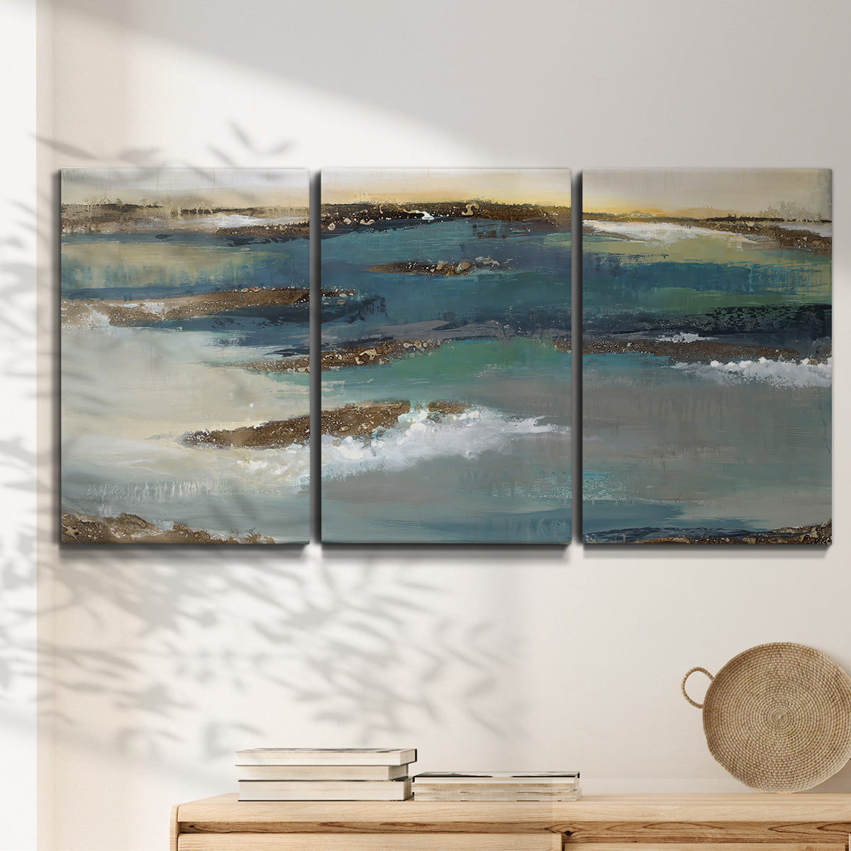 Three-panel canvas wall art featuring rocky coastal bluff above sea, displayed in a minimalist living room above a console table.