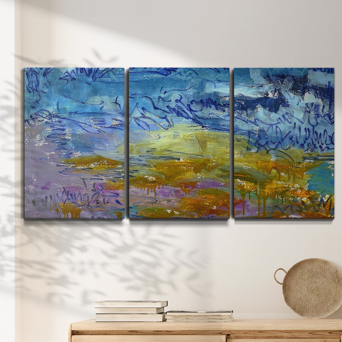 Three-panel canvas wall art featuring expressive abstract with layered color, displayed in a minimalist living room above a console table.