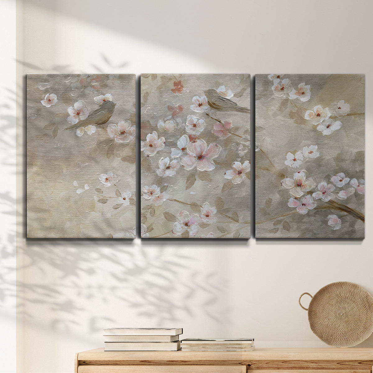 Three-panel canvas wall art featuring early spring blossoms in soft tones, displayed in a minimalist living room above a console table.