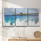Three-panel canvas wall art featuring coastal pier extending over water, displayed in a minimalist living room above a console table.