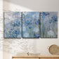 Three-panel canvas wall art featuring delicate watercolor floral blooms, displayed in a minimalist living room above a console table.