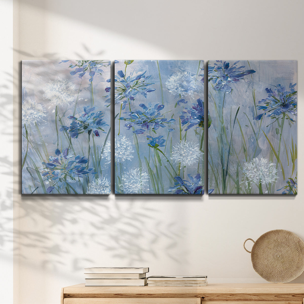 Three-panel canvas wall art featuring delicate watercolor floral blooms, displayed in a minimalist living room above a console table.