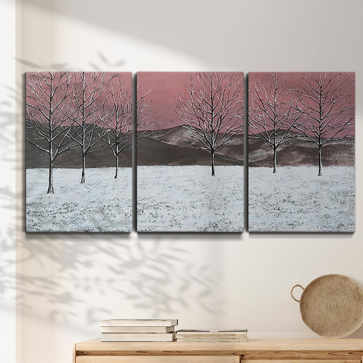 Three-panel canvas wall art featuring winter sunset snowfall landscape, displayed in a minimalist living room above a console table.