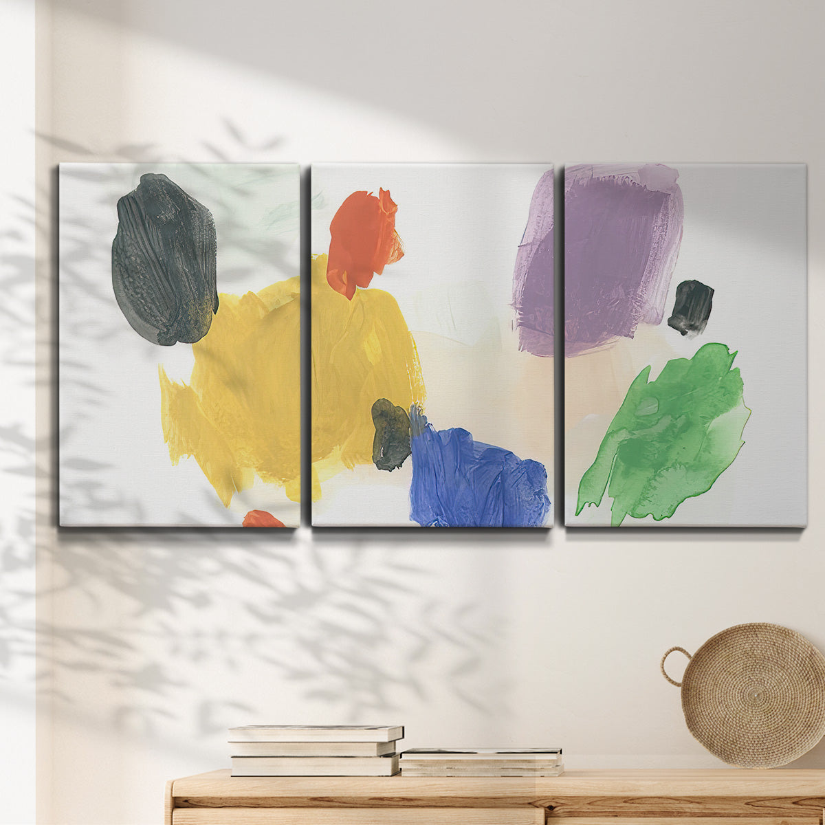 Three-panel canvas wall art featuring inkblot style abstract color symmetry, displayed in a minimalist living room above a console table.