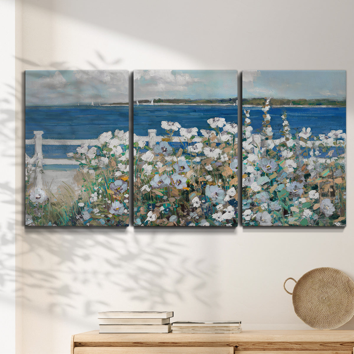 Three-panel canvas wall art featuring coastal garden overlooking bay, displayed in a minimalist living room above a console table.