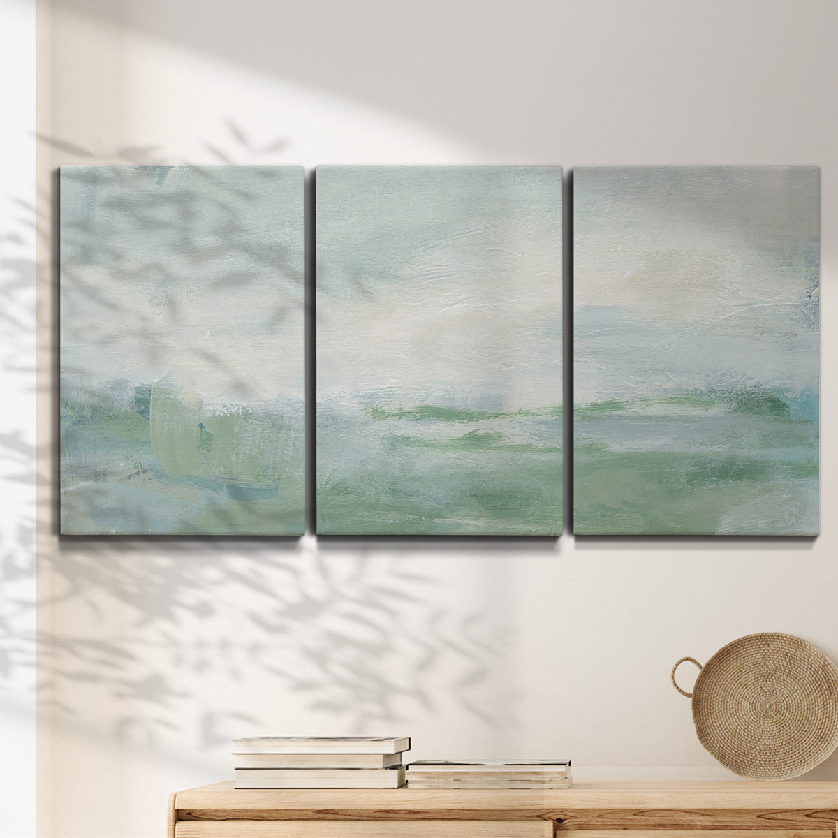 Three-panel canvas wall art featuring soft abstract coastal tones, displayed in a minimalist living room above a console table.