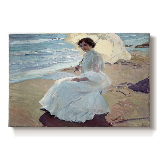 Canvas art print portraying a woman seated on beach in flowing white dress beside water, set against a white background