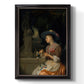 Classical interior scene of a woman weaving flowers by Godfried Schalcken printed on canvas in an ornate black frame with gilded inner detail with a vertical orientation.