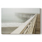 Fog envelops a pier while waves gently lap against the shore on a tranquil morning