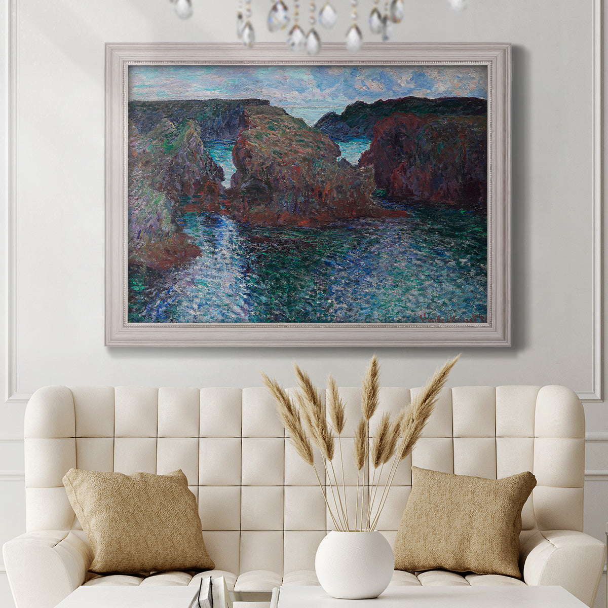 Impressionist rocky seascape by Claude Monet in an ornate weathered white frame displayed in a neutral-toned interior setting.