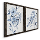 Angled view of a set of two black barnwood framed canvas prints featuring two expressive watercolor botanical paintings featuring loose blue flowers and leafy branches.