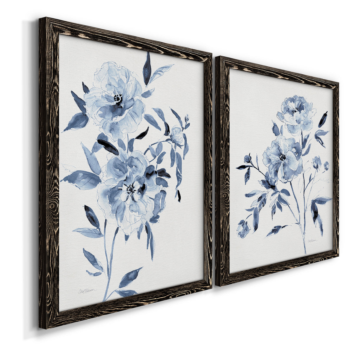 Angled view of a set of two black barnwood framed canvas prints featuring two expressive watercolor botanical paintings featuring loose blue flowers and leafy branches.