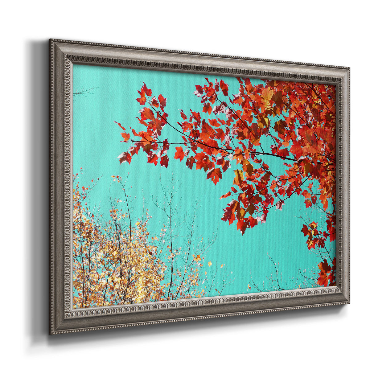 Red autumn leaves against a blue sky printed on canvas in an ornate vintage silver frame.