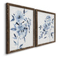 Angled view of a set of two walnut barnwood framed canvas prints featuring two expressive watercolor botanical paintings featuring loose blue flowers and leafy branches.