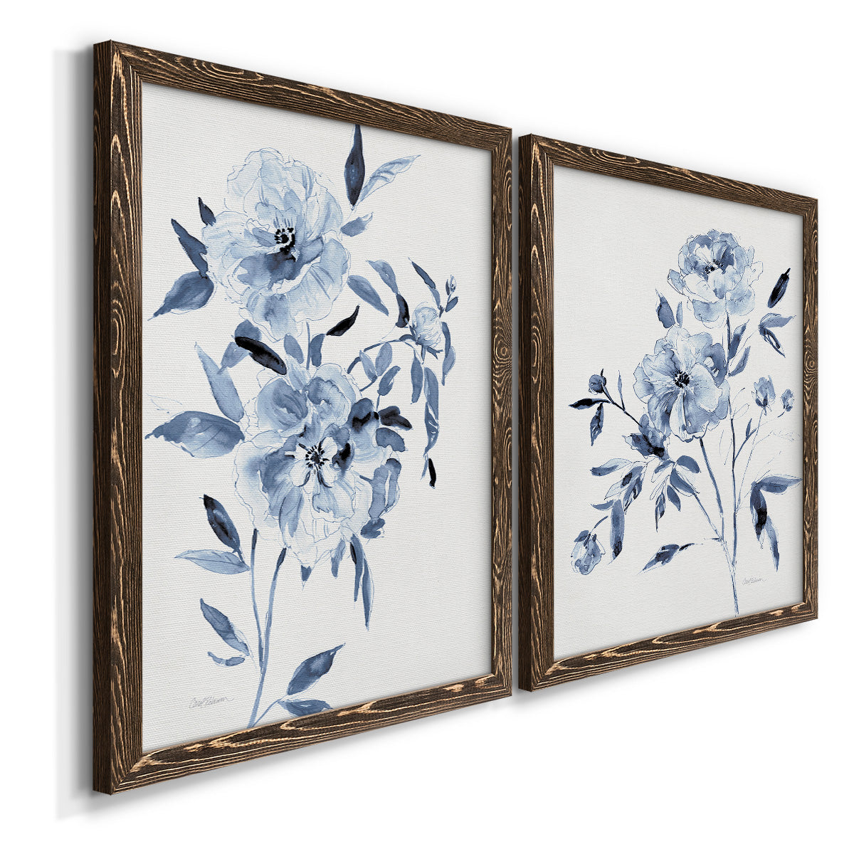 Angled view of a set of two walnut barnwood framed canvas prints featuring two expressive watercolor botanical paintings featuring loose blue flowers and leafy branches.