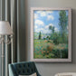 Impressionist pastoral landscape with poppy fields by Claude Monet in an ornate weathered white frame displayed in a neutral interior setting.