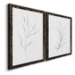 Angled view of a set of two black barnwood framed canvas prints featuring two minimalist botanical line drawings featuring single continuous-line leafy branches.