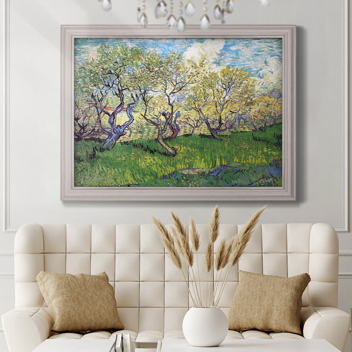 Impressionist spring orchard landscape by Vincent van Gogh in an ornate weathered white frame displayed in a neutral-toned interior setting.