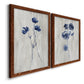 Angled view of a set of two maple barnwood framed canvas prints featuring two rustic monochrome botanical paintings featuring blue wildflower stems on weathered neutral paper.