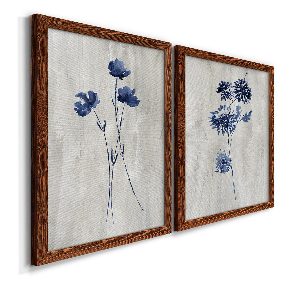 Angled view of a set of two maple barnwood framed canvas prints featuring two rustic monochrome botanical paintings featuring blue wildflower stems on weathered neutral paper.