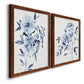 Angled view of a set of two maple barnwood framed canvas prints featuring two expressive watercolor botanical paintings featuring loose blue flowers and leafy branches.