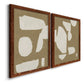 Angled view of a set of two maple barnwood framed canvas prints featuring two bold minimalist shape abstracts featuring irregular white cutout-like shapes on taupe grounds.