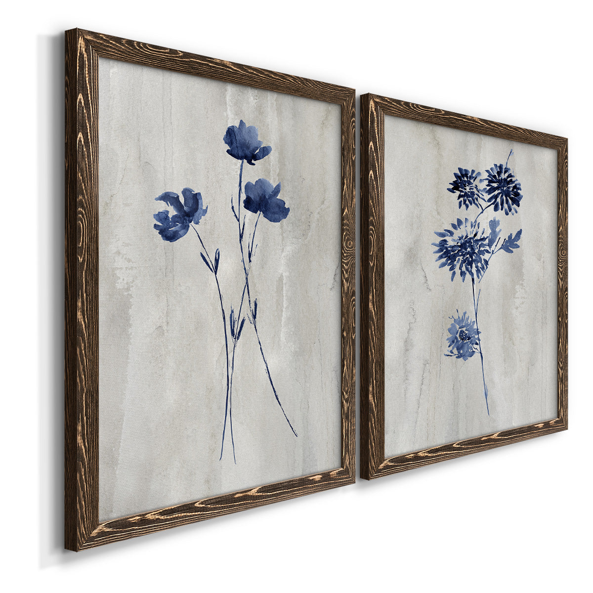Angled view of a set of two walnut barnwood framed canvas prints featuring two rustic monochrome botanical paintings featuring blue wildflower stems on weathered neutral paper.