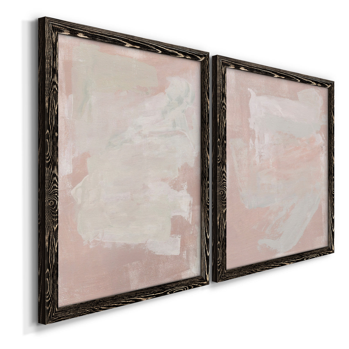 Angled view of a set of two black barnwood framed canvas prints featuring two minimalist color-field abstracts featuring soft blush and white painterly fields.