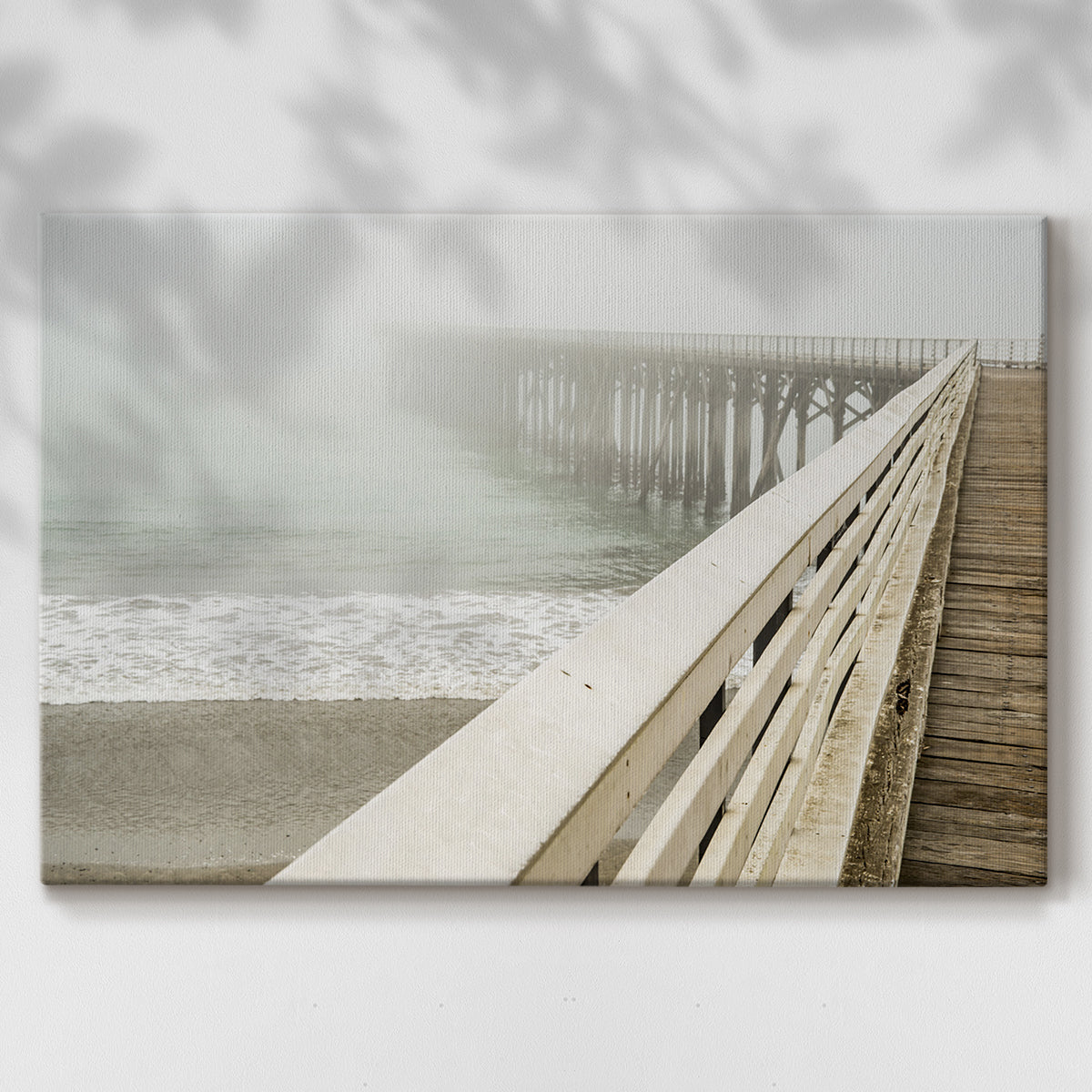 Fog envelops a pier while waves gently lap against the shore on a tranquil morning