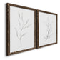 Angled view of a set of two walnut barnwood framed canvas prints featuring two minimalist botanical line drawings featuring single continuous-line leafy branches.