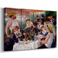 Canvas art print featuring a lively gathering of men and women eating and socializing at outdoor table, displayed at an angle