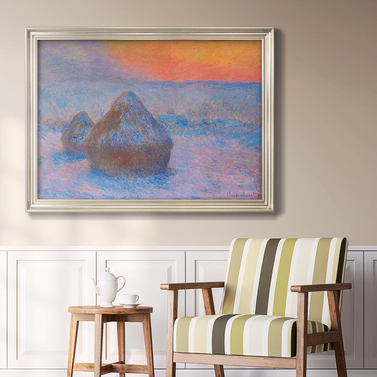 Impressionist haystack scene at sunset by Claude Monet in an ornate champagne frame displayed in a light-toned interior setting.