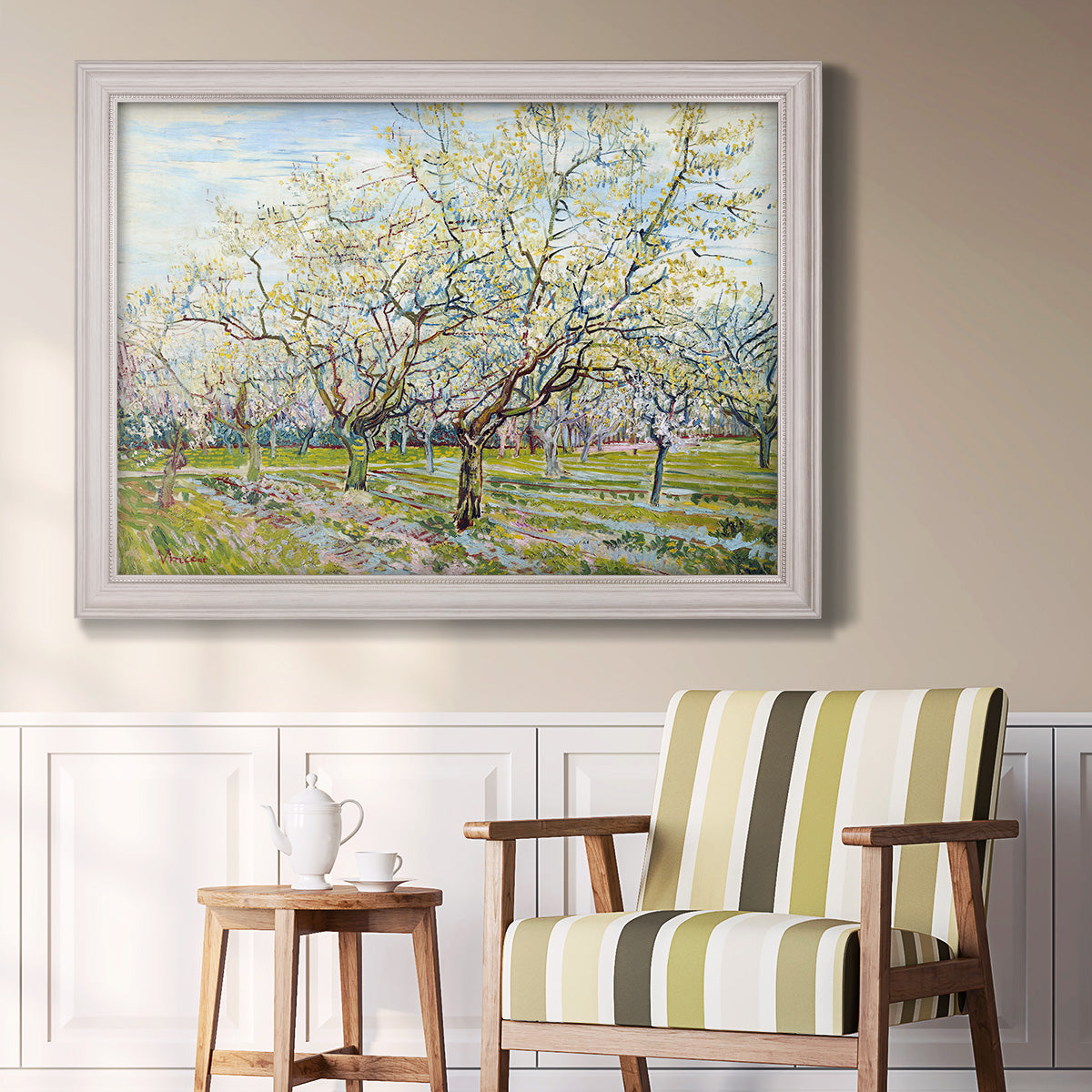 Impressionist white-blossomed orchard landscape by Vincent van Gogh in an ornate weathered white frame displayed in a light-toned interior setting.