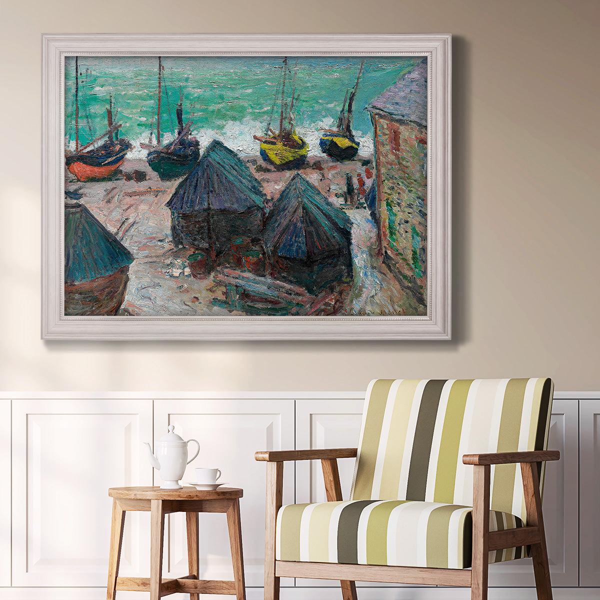 Impressionist coastal beach scene with boats by Claude Monet in an ornate weathered white frame displayed in a light-toned interior setting.