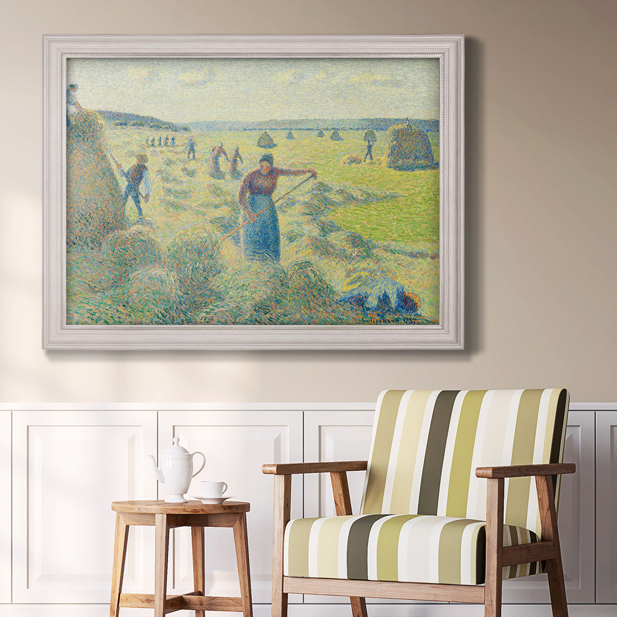 Impressionist rural hay harvest landscape by Camille Pissarro in an ornate weathered white frame displayed in a light-toned interior setting.