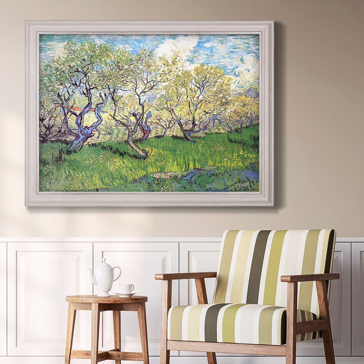 Impressionist spring orchard landscape by Vincent van Gogh in an ornate weathered white frame displayed in a light-toned interior setting.