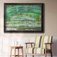 Impressionist garden scene with Japanese bridge and water lilies by Claude Monet in an ornate black frame with gilded inner detail displayed in a light-toned interior setting.