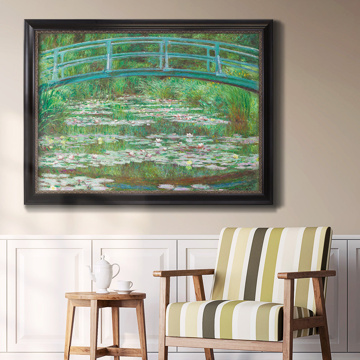 Impressionist garden scene with Japanese bridge and water lilies by Claude Monet in an ornate black frame with gilded inner detail displayed in a light-toned interior setting.