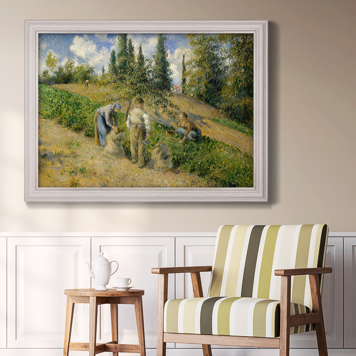 Impressionist countryside harvest scene by Camille Pissarro in an ornate weathered white frame displayed in a light-toned interior setting.