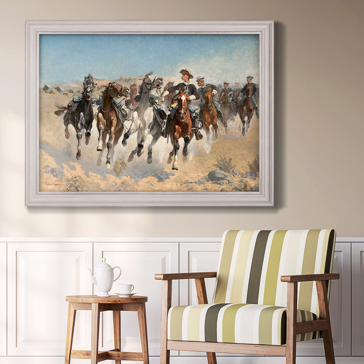 Impressionist western action scene by Frederic Remington in an ornate weathered white frame displayed in a light-toned interior setting.