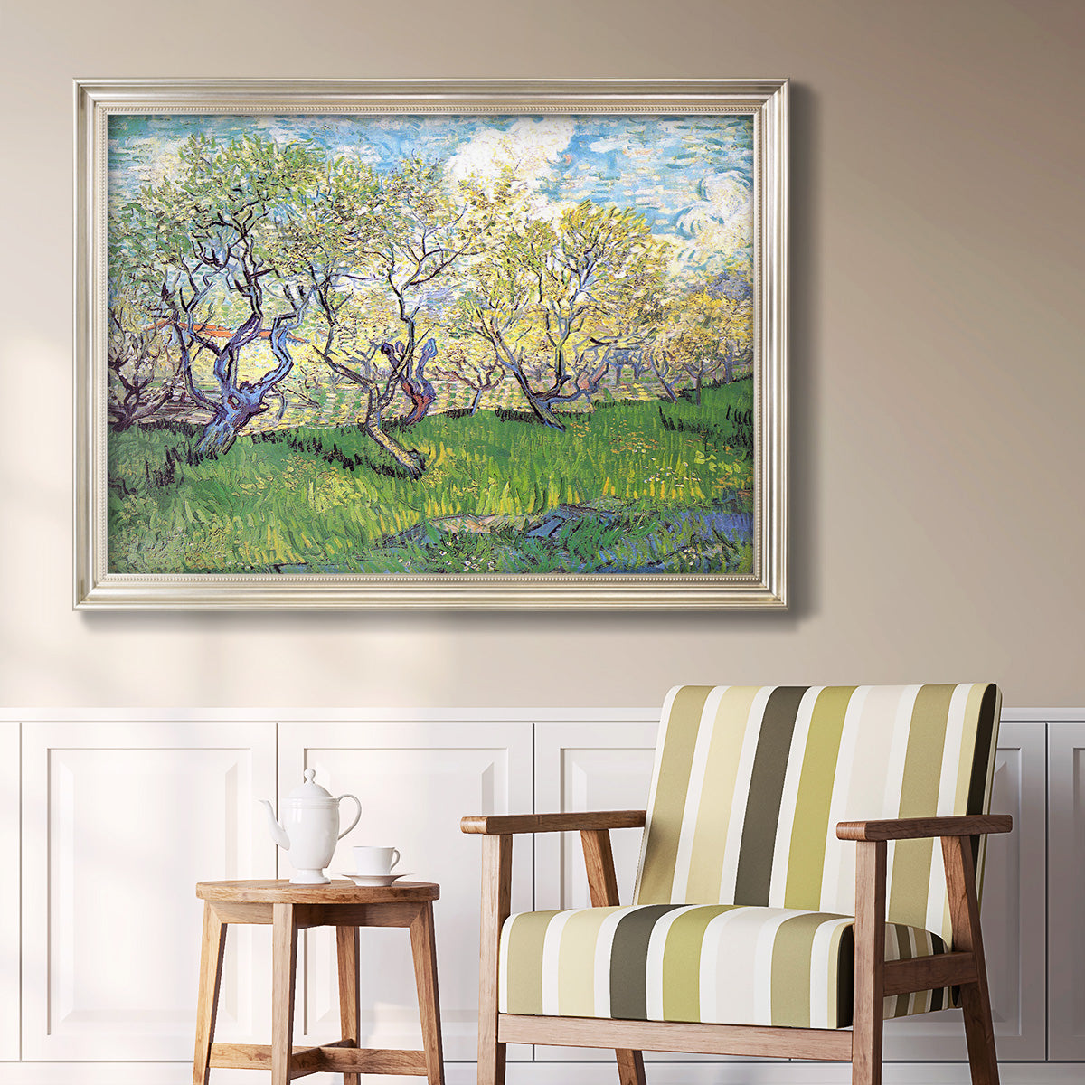 Impressionist spring orchard landscape by Vincent van Gogh in an ornate champagne frame displayed in a light-toned interior setting.