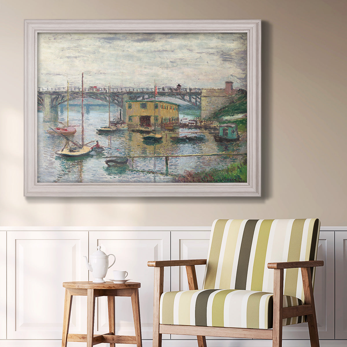 Impressionist river bridge scene on an overcast day by Claude Monet in an ornate weathered white frame displayed in a light-toned interior setting.