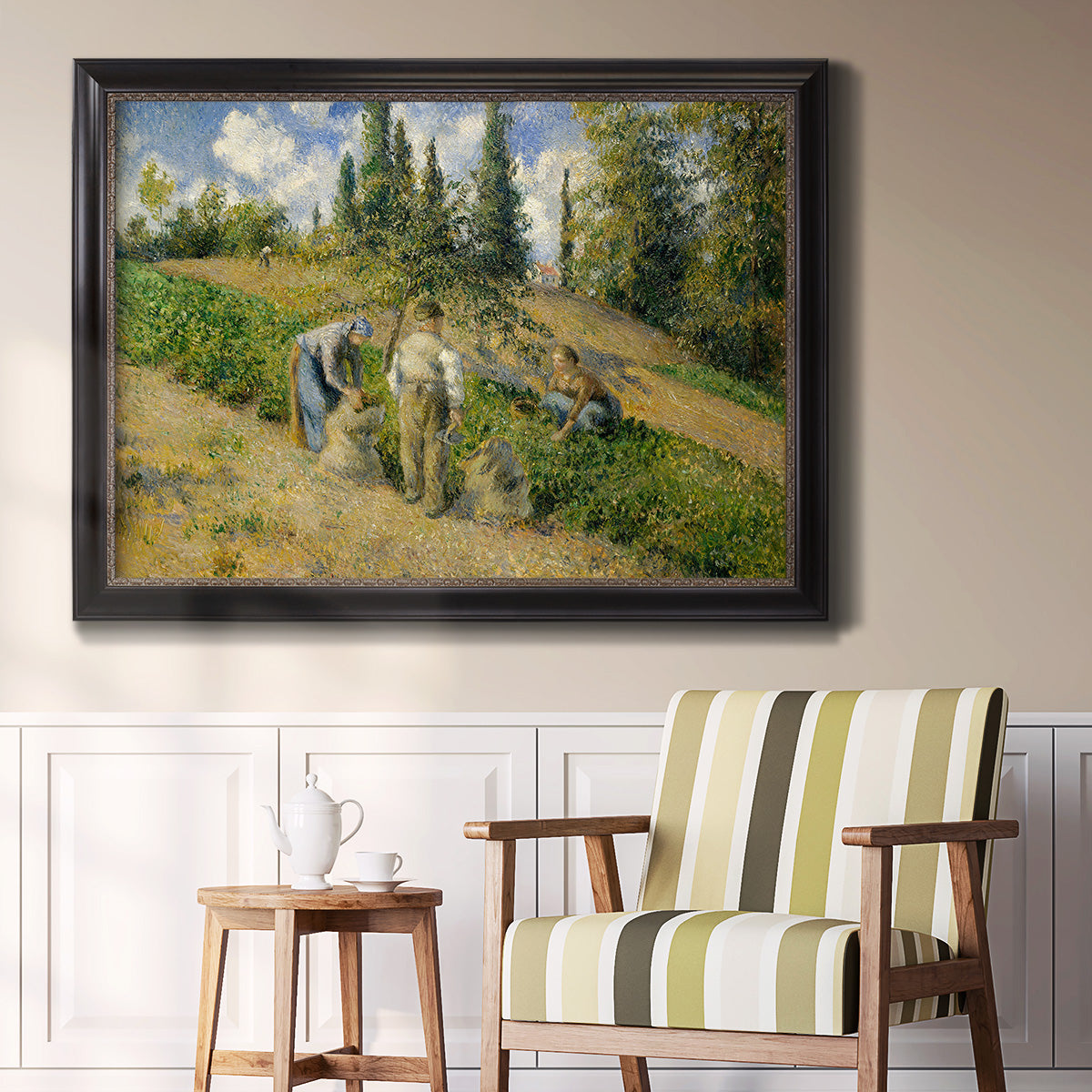 Impressionist countryside harvest scene by Camille Pissarro in an ornate black frame with gilded inner detail displayed in a light-toned interior setting.