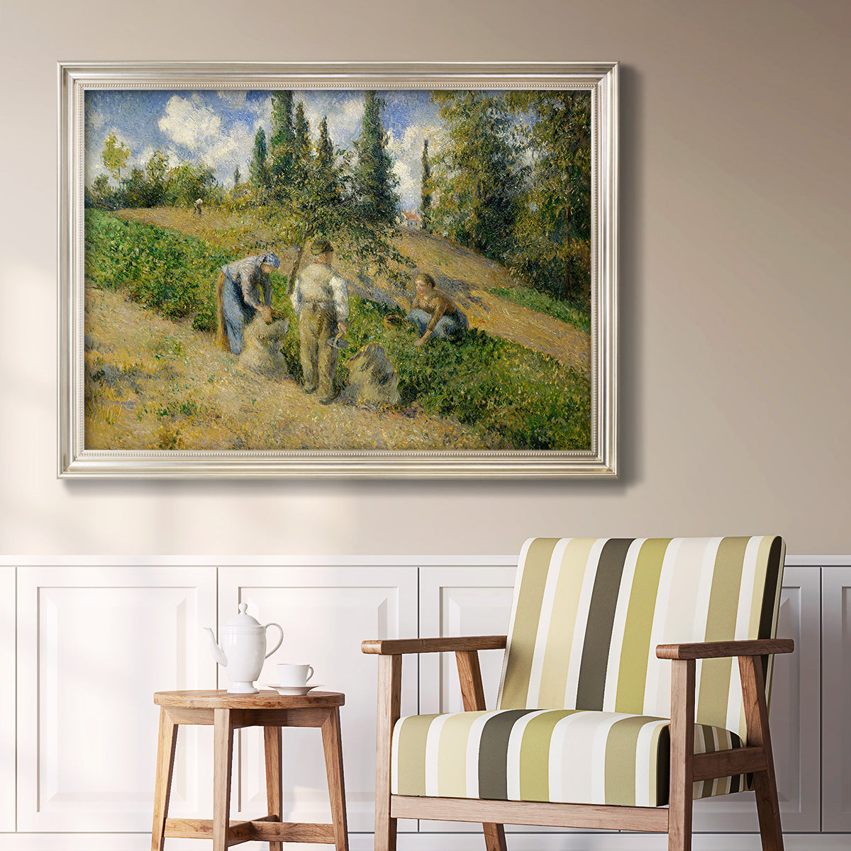 Impressionist countryside harvest scene by Camille Pissarro in an ornate champagne frame displayed in a light-toned interior setting.