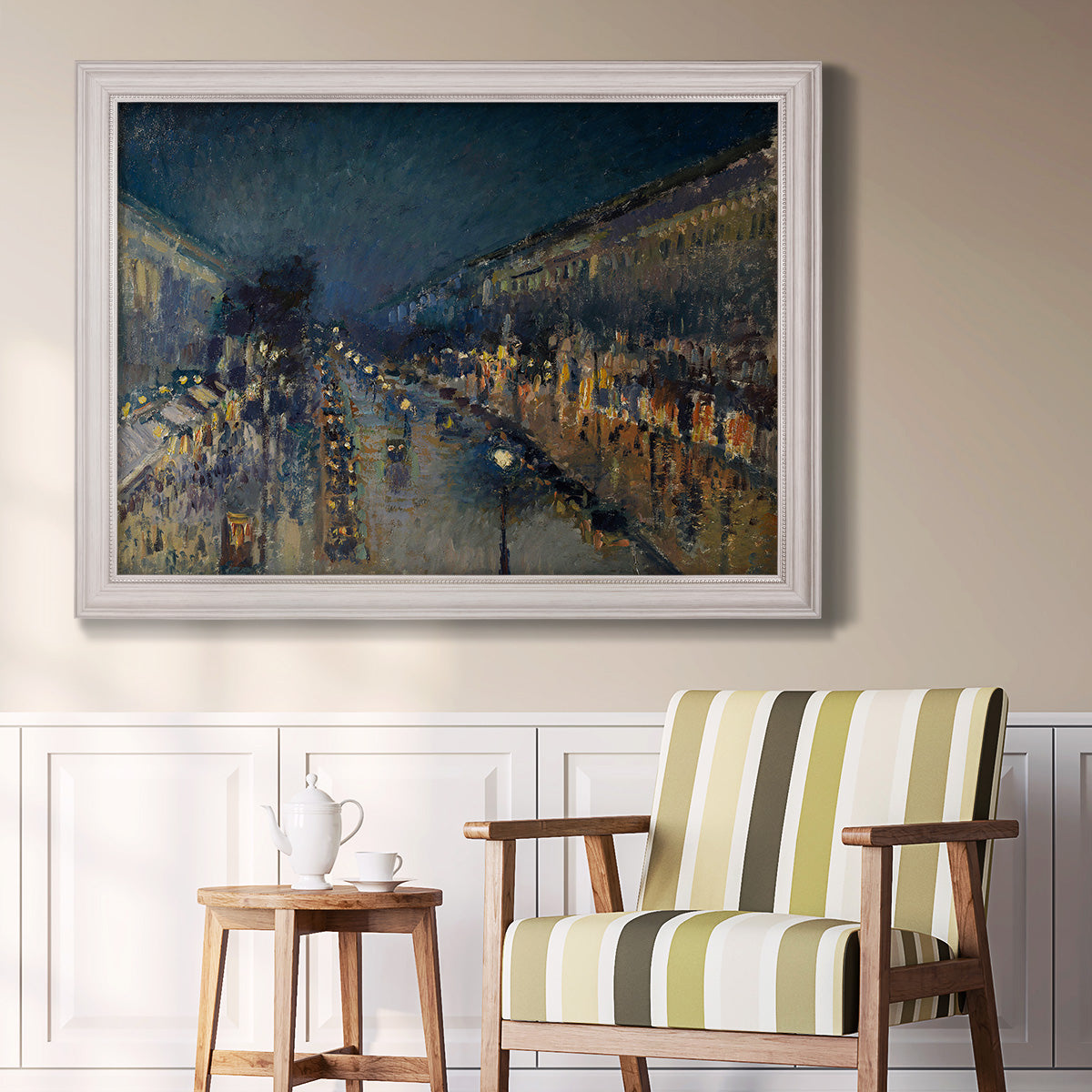 Impressionist nighttime Paris street scene by Camille Pissarro in an ornate weathered white frame displayed in a light-toned interior setting.