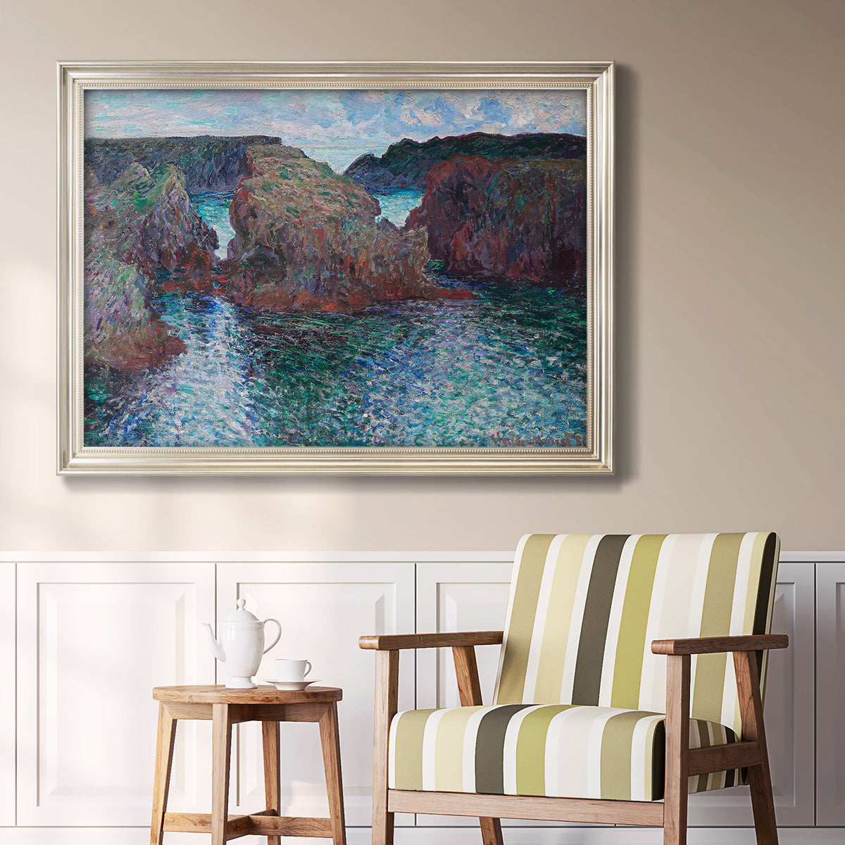 Impressionist rocky seascape by Claude Monet in an ornate champagne frame displayed in a light-toned interior setting.