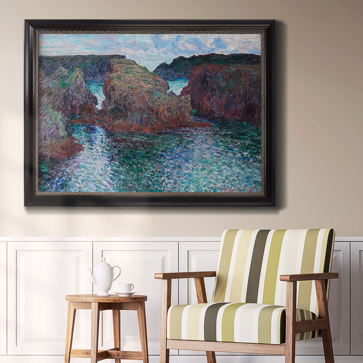 Impressionist rocky seascape by Claude Monet in an ornate black frame with gilded inner detail displayed in a light-toned interior setting.