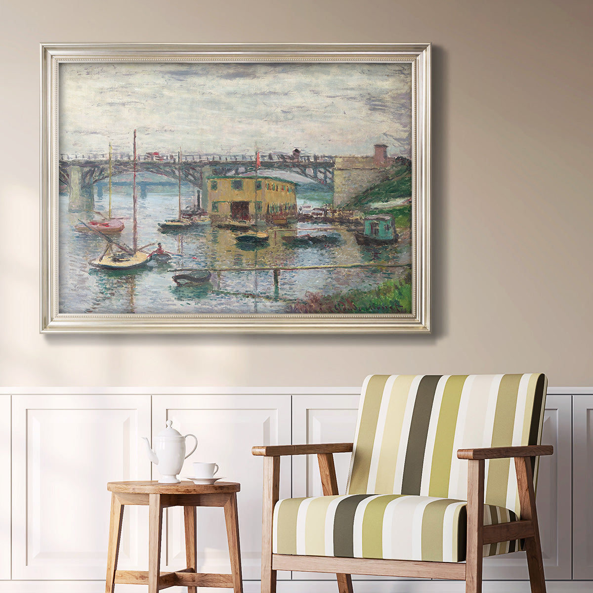 Impressionist river bridge scene on an overcast day by Claude Monet in an ornate champagne frame displayed in a light-toned interior setting.