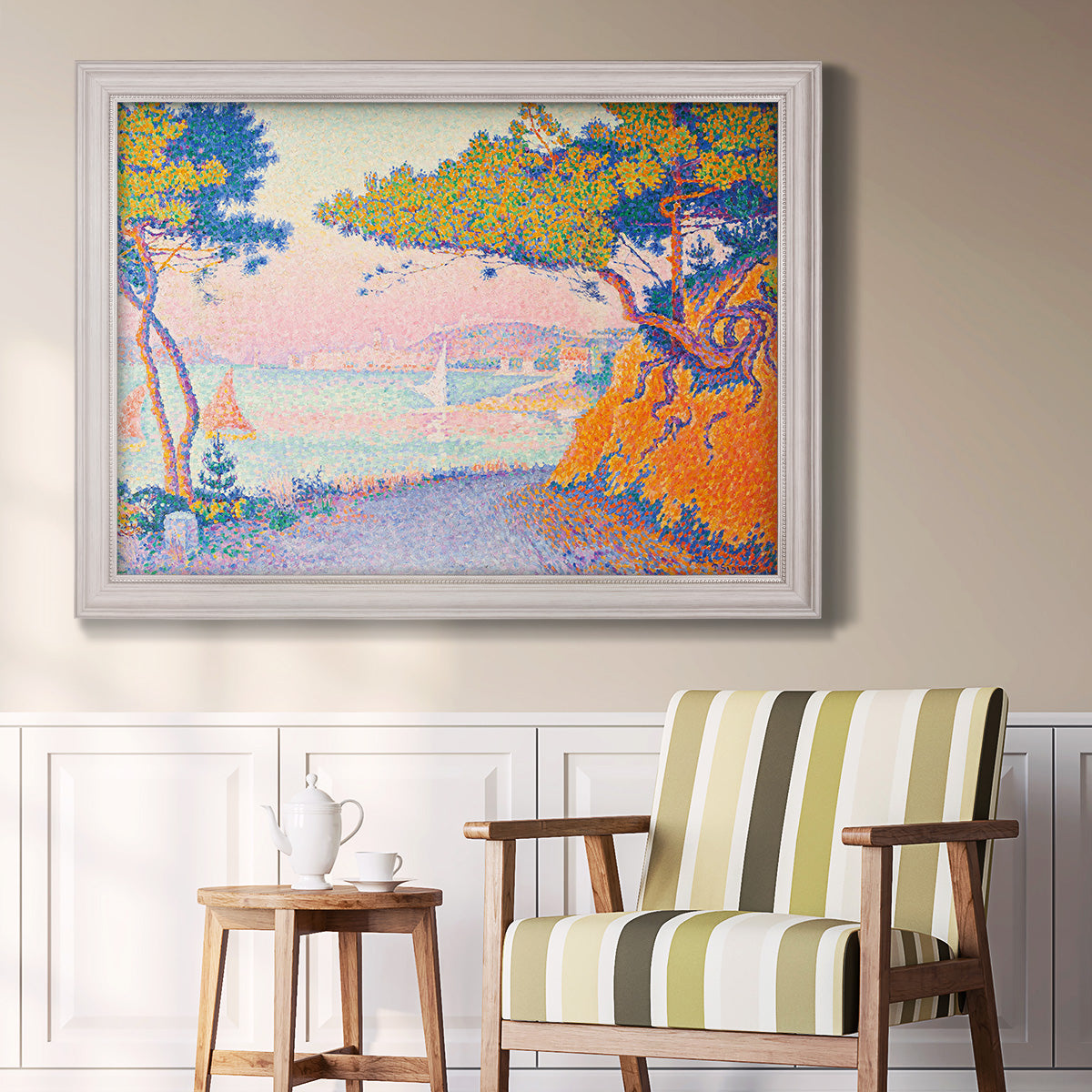 Pointillist coastal seascape by Paul Signac in an ornate weathered white frame displayed in a light-toned interior setting.