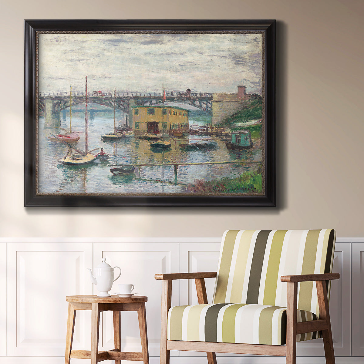 Impressionist river bridge scene on an overcast day by Claude Monet in an ornate black frame with gilded inner detail displayed in a light-toned interior setting.